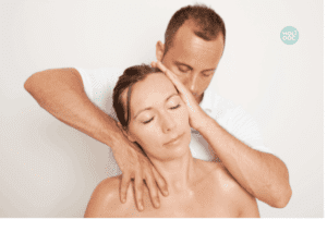 un homme en tee shirt blanc manipule la tête et le cou d'une femme assise devant lui