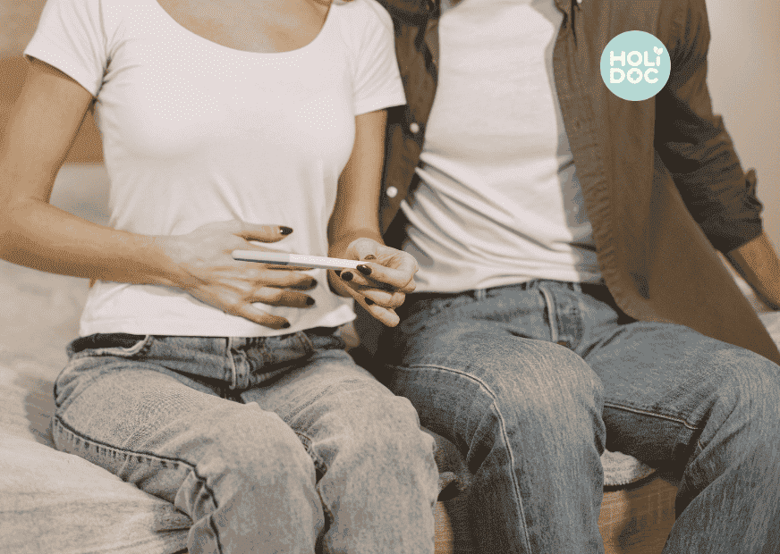 une femme assise à côté de son mari et se tenant le ventre regarde les résultats d'un test de grossesse