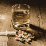 un verre rempli d'alcool est posée sur une table en bois, à côté de médicaments et d'une seringue