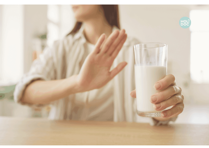 une femme tient un verre de lait et fait signe de l'autre main qu'elle n'en veut pas