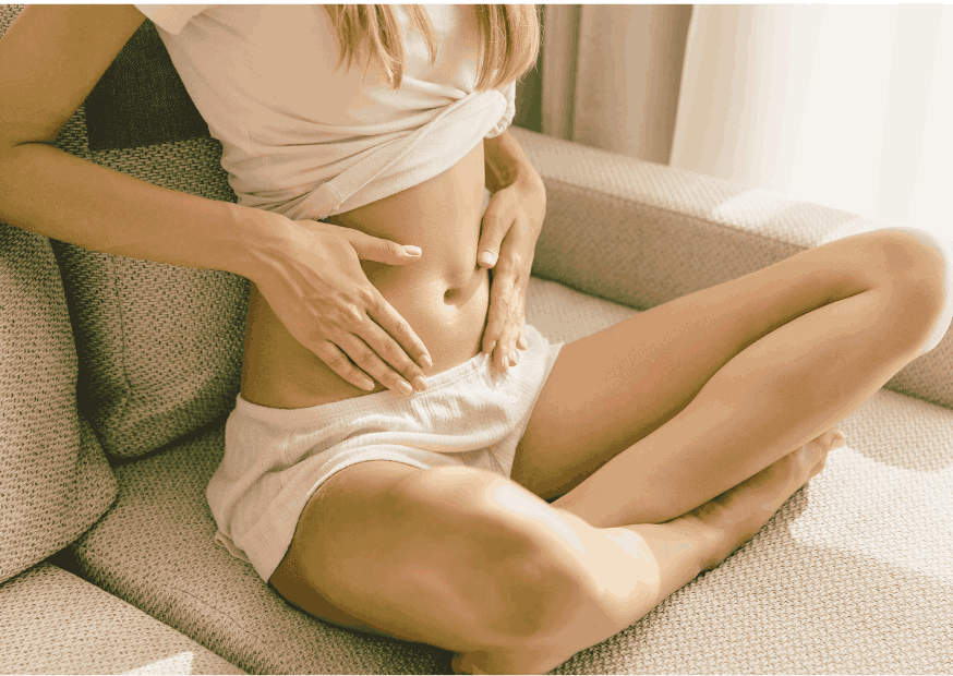 femme assise en tailleur sur son canapé, ventre à l'air et les mains posées sereinement dessus