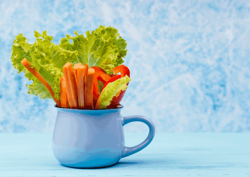tasse bleue sur fond bleu, remplie de feuilles de salades, et morceaux de poivrons rouges.