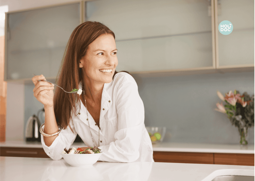 triglycérides-min femme souriante mangeant une salade devant le comptoir de sa cuisine