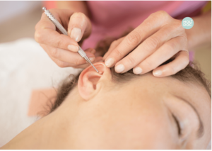 une femme pointe une aiguille vers l'oreille d'une femme allongée les yeux fermés